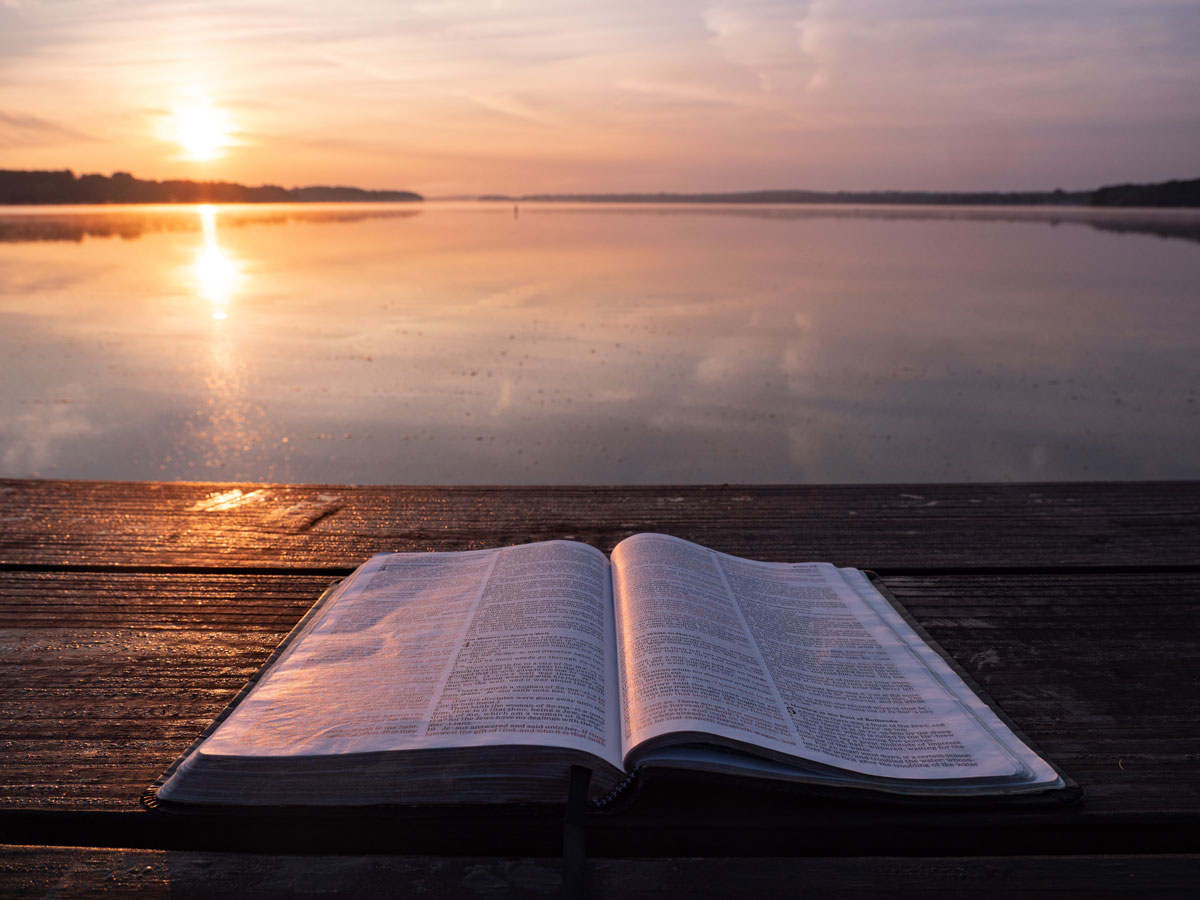 Open Bible on wooden table with lake view in the background